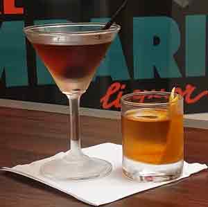 Martini and whiskey glasses filled with drinks on table with cocktail napkin.